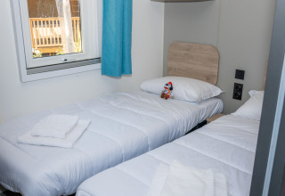 Zwei Einzelbetten in einem hellen Zimmer mit Fenster, blauen Vorhängen und Handtüchern im Trasimeno Glamping Resort.