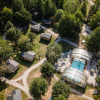 Aerial view of Huttopia Les Chateaux - Glamping Val de Loire with cabins, a pool, and lush green trees.