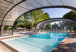 Überdachtes Schwimmbad mit Holzboden im Huttopia Les Chateaux - Glamping Val de Loire, umgeben von Natur.