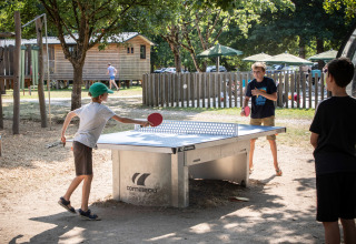 Des enfants jouent au ping-pong en plein air à Huttopia Les Chateaux - Glamping Val de Loire, avec des cabanes.
