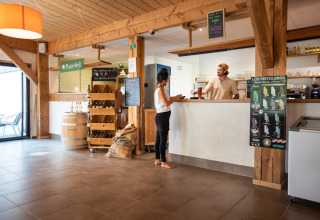 Reception area of Huttopia Les Châteaux - Glamping Val de Loire with guest talking to staff, wooden decor.