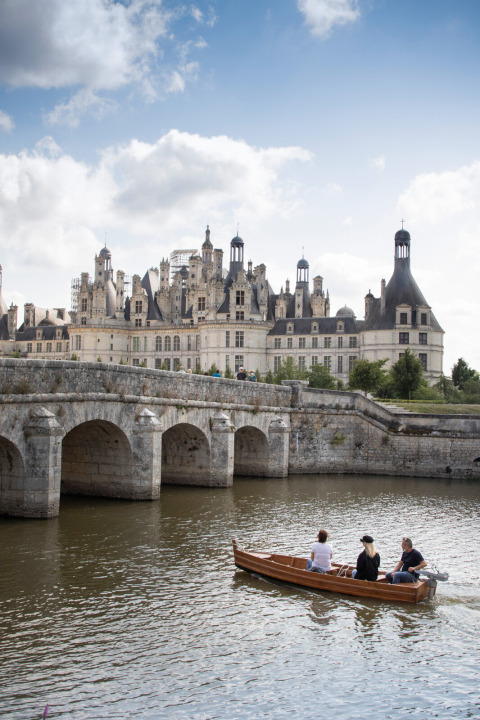 Drie mensen varen in een bootje op de rivier voor een kasteel bij Huttopia Les Chateaux - Glamping Val de Loire.