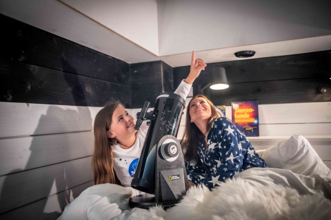 Due persone in pigiama stellato osservano il cielo con un telescopio nel glamping Sterrenkubussen Twente.