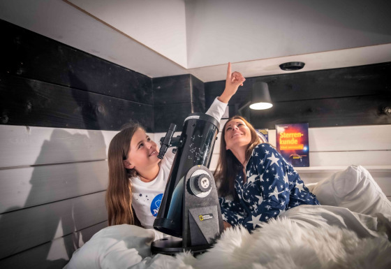 Twee personen in sterrenpyjama’s bekijken de sterren door een telescoop in Sterrenkubussen Twente glamping.