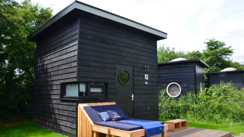 Cabane glamping noire moderne à Erfgoed Bossem - Sterrenkubussen Twente, entourée de verdure et d’arbres.