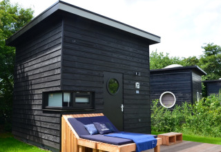 Cabane glamping noire moderne à Erfgoed Bossem - Sterrenkubussen Twente, entourée de verdure et d’arbres.