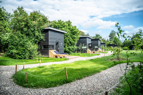Glamping cabins at Erfgoed Bossem - Sterrenkubussen Twente, nestled in greenery and nature under a blue sky.