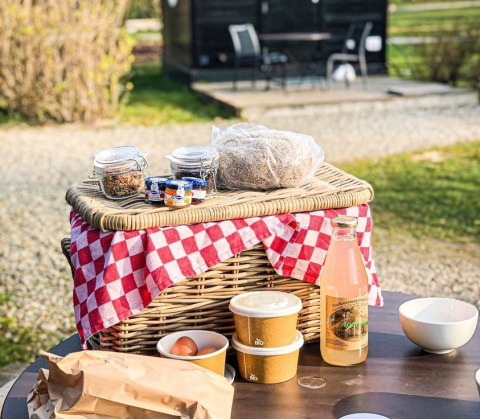 Breakfast picnic basket and drinks on table outside glamping at Erfgoed Bossem - Sterrenkubussen Twente.