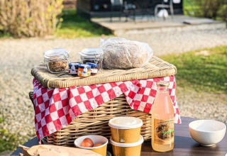 Frühstückskorb mit Getränken und Speisen auf Tisch vor Glamping bei Erfgoed Bossem - Sterrenkubussen Twente.