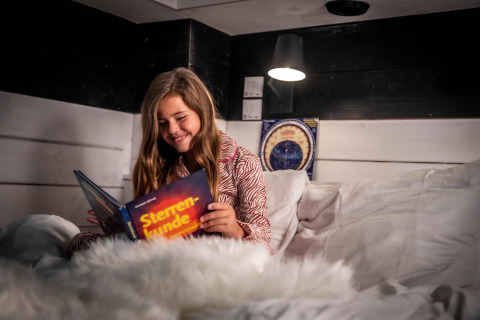 Meisje leest in bed in een Sterrenkubus bij Erfgoed Bossem - Sterrenkubussen Twente, glamping.