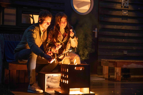 Pareja disfrutando de glamping junto a una fogata frente a una cabaña en Erfgoed Bossem - Sterrenkubussen Twente.