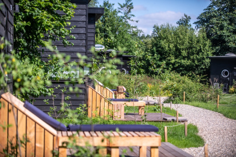 Buitenaanzicht van glamping accommodatie bij Erfgoed Bossem - Sterrenkubussen Twente met groen en houten banken.