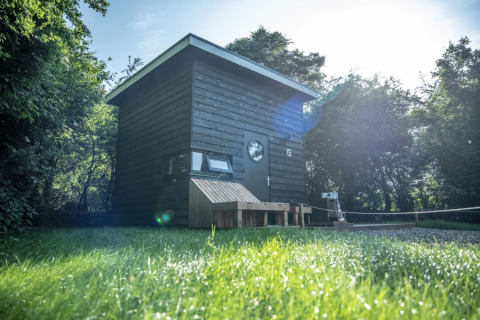 Moderne schwarze Glamping-Hütte namens Sterrenkubus im Erfgoed Bossem, Twente, umgeben von grünem Gras.