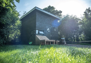 Cabane en bois noire moderne pour glamping nommée Sterrenkubus à Erfgoed Bossem, Twente, entourée d’herbe verte.