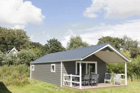 Strand49 - Strandlodges & Cabins Noord-Holland: cabaña glamping con terraza, sillas y entorno verde natural.