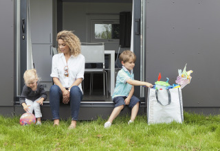 Gezin geniet buiten aan Strand49 glamping lodge in Noord-Holland, kinderen spelen met speelgoed op het gras.