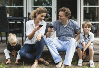 Familia disfruta en la terraza de una cabaña en Strand49, Noord-Holland, padres con vino y niños jugando.