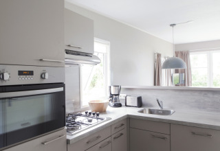 Moderne keuken in een Strand49 lodge in Noord-Holland met oven, fornuis, gootsteen en koffiezetapparaat.