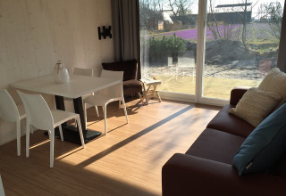 Moderne glampingaccommodatie met eetafel, bank en groot raam met uitzicht in Noord-Holland.