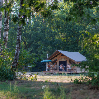 Glamping au Camping Huttopia De Meinweg dans le Limbourg, Pays-Bas, avec des personnes devant une tente safari.