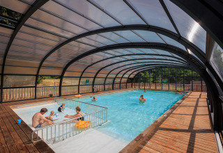 Overdækket swimmingpool med familier, der nyder vandet på Camping Huttopia De Meinweg Glamping Limburg.