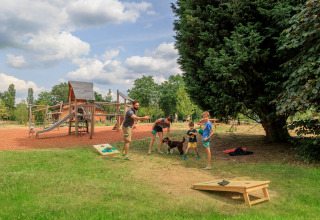 Familie leger cornhole og børn leger på legeplads ved Camping Huttopia De Meinweg - Glamping Limburg.
