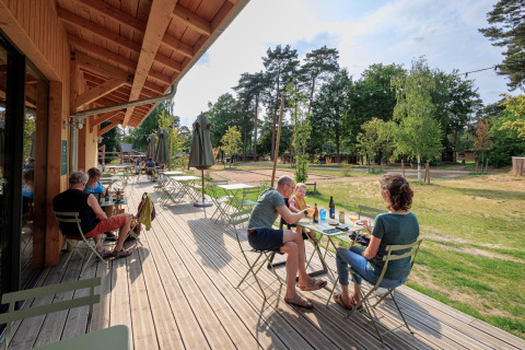 Terrasse des Camping Huttopia De Meinweg - Glamping Limburg mit Gästen und Blick auf die Natur.
