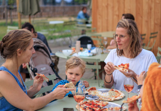 En familie nyder pizza sammen udenfor på Camping Huttopia De Meinweg - Glamping Limburg, Holland.