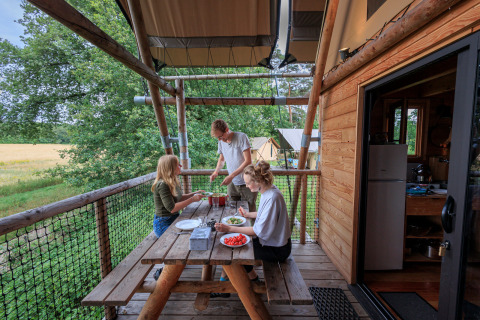 Mensen eten samen op een houten veranda bij Camping Huttopia De Meinweg - Glamping Limburg accommodatie.