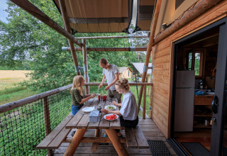 People enjoying a meal on a wooden terrace at Camping Huttopia De Meinweg - Glamping Limburg accommodation.