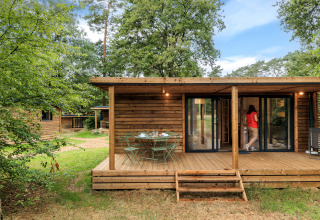 Blokhut bij Camping Huttopia De Meinweg - Glamping Limburg met veranda en buitentafel in groene omgeving.
