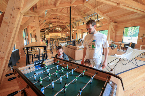 Family enjoying a foosball game inside a modern wooden lodge at Camping Huttopia De Meinweg - Glamping Limburg.