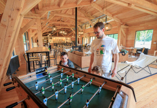 Gezin speelt tafelvoetbal in een houten lodge bij Camping Huttopia De Meinweg - Glamping Limburg.