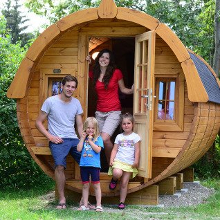 Family in front of a unique barrel-shaped glamping hut at Camping Heidehof, Glamping Baden-Württemberg.