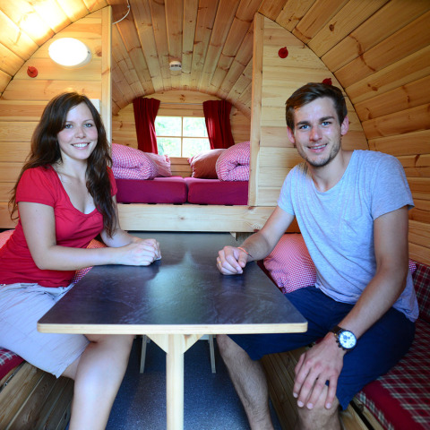 Two young adults sit inside a cozy, wooden glamping pod at Camping Heidehof, Baden-Württemberg, Germany.