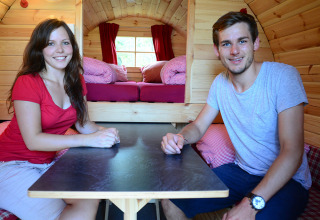 Two young adults sit inside a cozy, wooden glamping pod at Camping Heidehof, Baden-Württemberg, Germany.