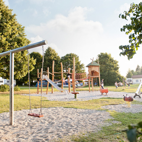 Playground at Camping Heidehof Glamping Baden-Württemberg with slide, swings, kids, and green surroundings.