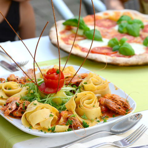 Plato de pasta con camarones y pizza al fondo servido en Camping Heidehof - Glamping Baden-Württemberg.