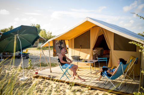Deux personnes se détendent devant une tente glamping sur le sable à Huttopia Côte Sauvage - Ile de Ré.