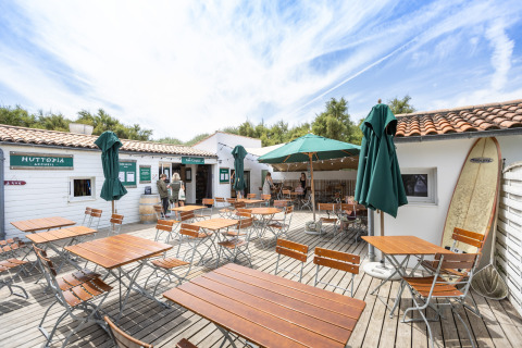 Terrasse extérieure du Huttopia Côte Sauvage - Ile de Ré glamping en Nouvelle-Aquitaine, avec tables et parasols.