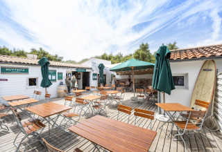 Außencafé bei Huttopia Côte Sauvage - Ile de Ré Glamping in Nouvelle-Aquitaine mit Holztischen und Sonnenschirmen.