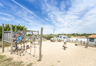 Children playing on a sandy playground with climbing net at Huttopia Côte Sauvage - Ile de Ré glamping site.