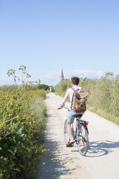 A person rides a bicycle down a dirt path at Huttopia Côte Sauvage - Ile de Ré - Glamping Nouvelle-Aquitaine.