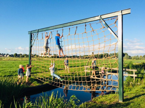 Bambini che si arrampicano su una grande rete di corde all'aperto a Boerderij De Boerinn – Safaritenten Utrecht.