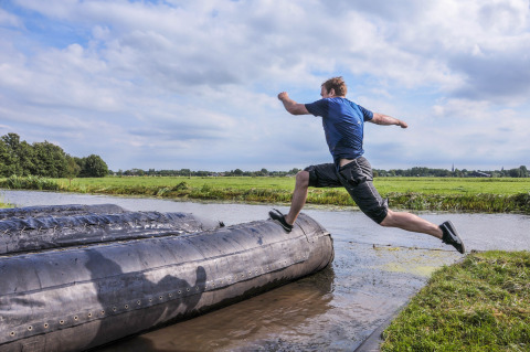 Hombre salta sobre un gran obstáculo inflable en Boerderij De Boerinn – Safaritenten Utrecht, rodeado de campos verdes.