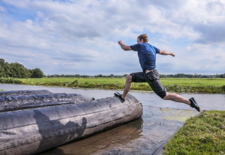 Man jumps over a large inflatable obstacle at Boerderij De Boerinn – Safaritenten Utrecht, surrounded by green fields.