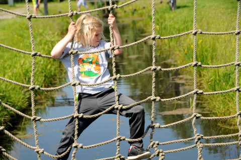 Child climbing a rope net over water at Boerderij De Boerinn – Safaritenten Utrecht, glamping in Holland.