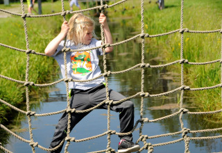 Kind klimt over een touwnet boven water bij Boerderij De Boerinn – Safaritenten Utrecht, glamping Nederland.