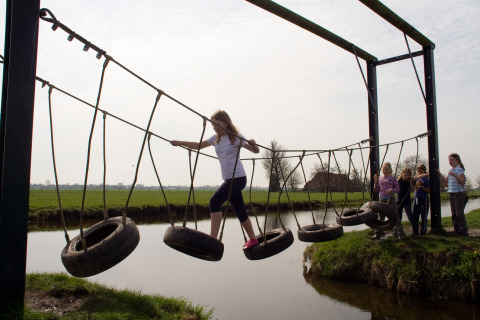 Niños cruzan un puente colgante de neumáticos sobre el agua en Boerderij De Boerinn – Safaritenten Utrecht.