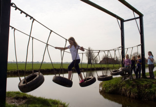 Kinderen lopen over een hangbrug van autobanden boven water bij Boerderij De Boerinn – Safaritenten Utrecht.